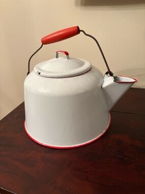 vintage white porcelain enamelware kettle with red trim and a red handle.